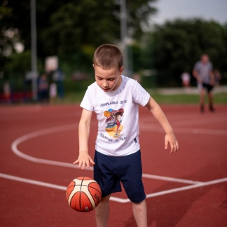 Škola košarke za decu, dečak se igra na terenu sa košarkaškom loptom u sportanac majicama